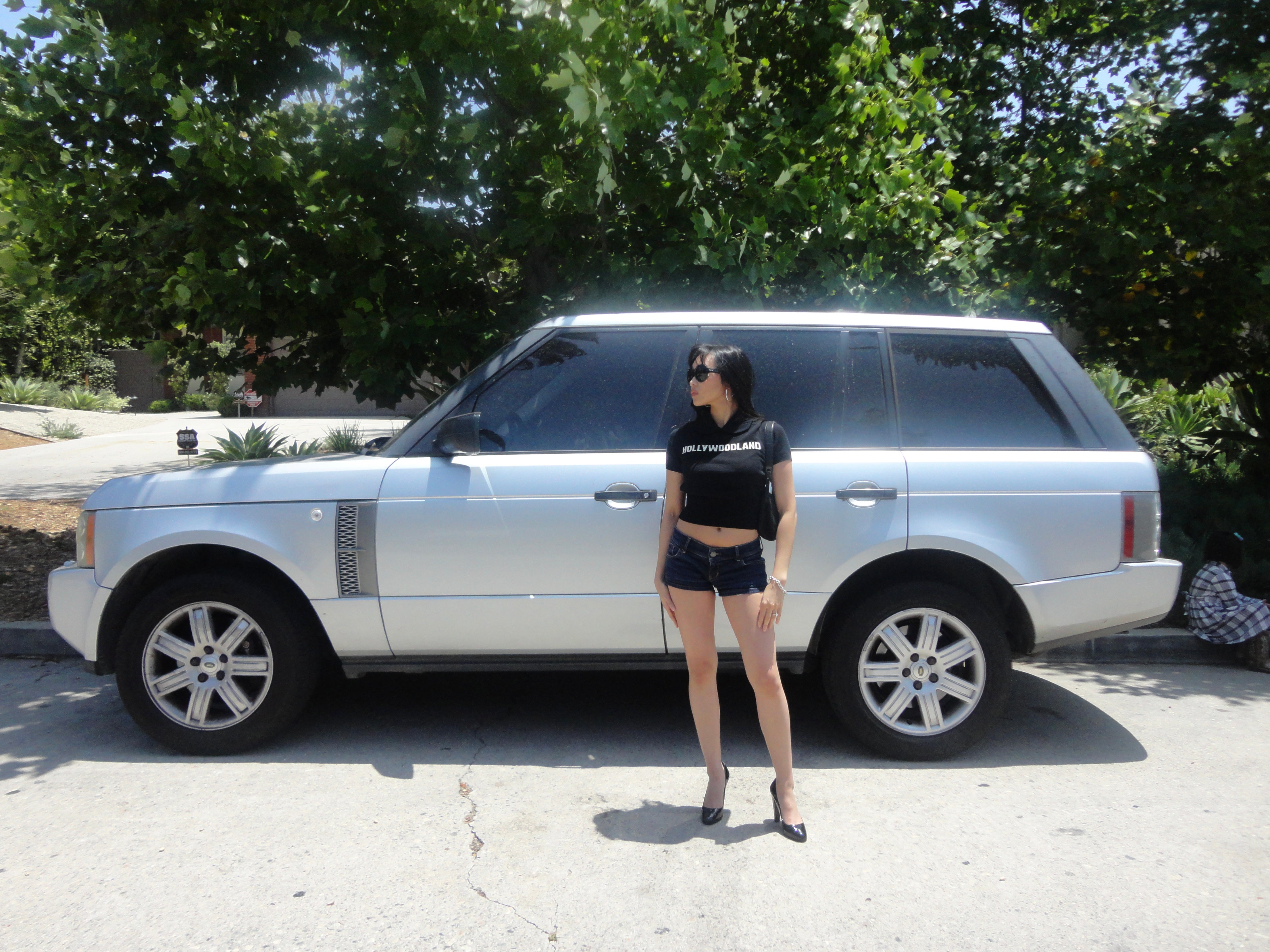 Woman standing next to a silver Range Rover with trees in the background